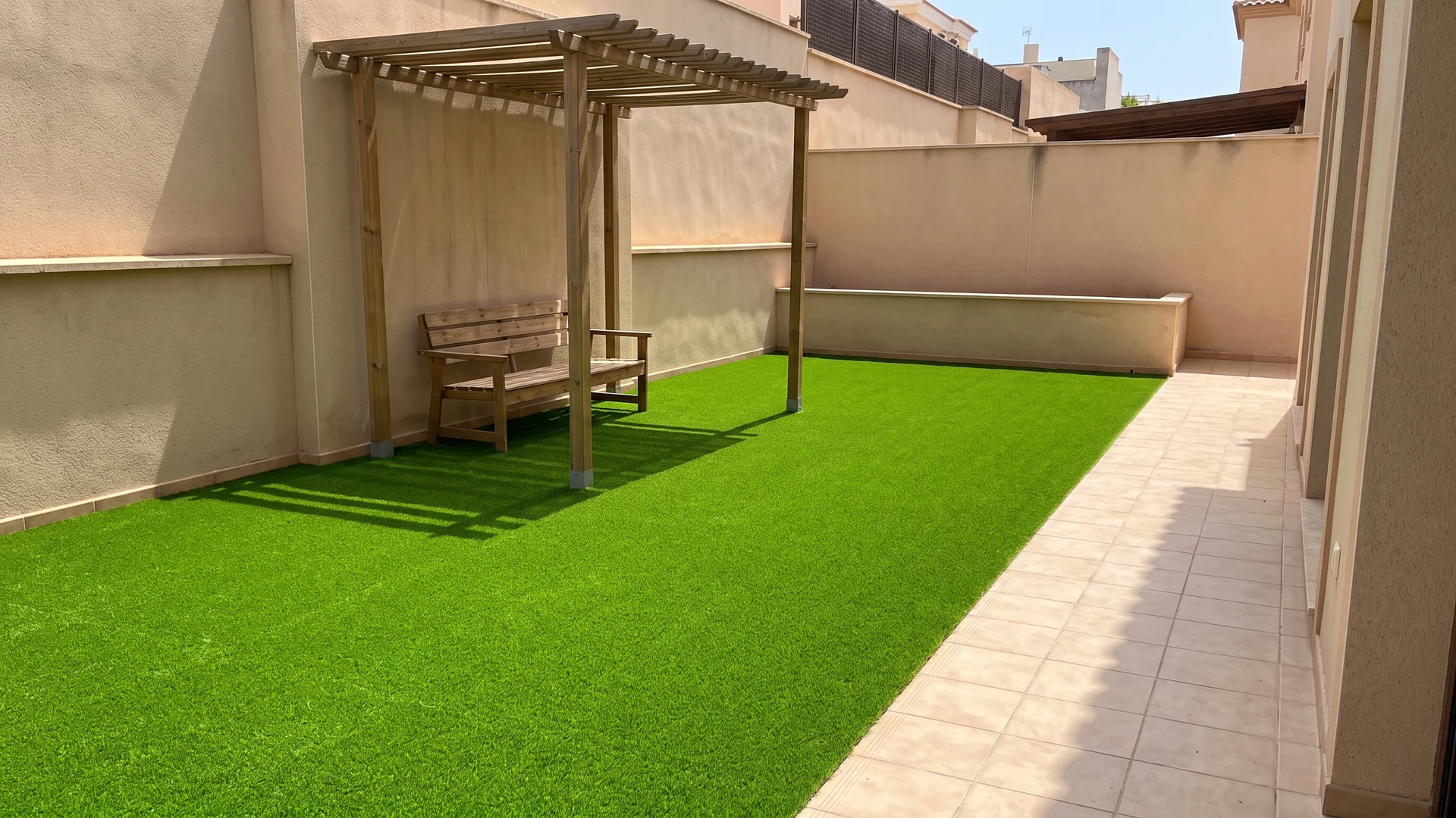 Patio con césped artificial, pérgola de madera y banco Patio con césped artificial, pérgola de madera y banco.
