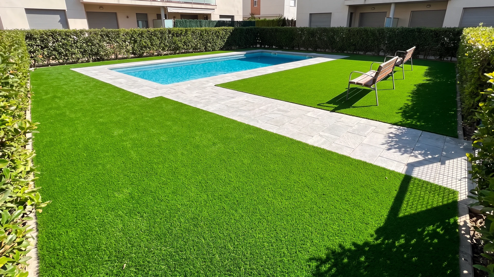 Jardín comunitario con césped artificial, piscina y bancos entre setos Jardín comunitario con césped artificial, piscina y bancos entre setos.
