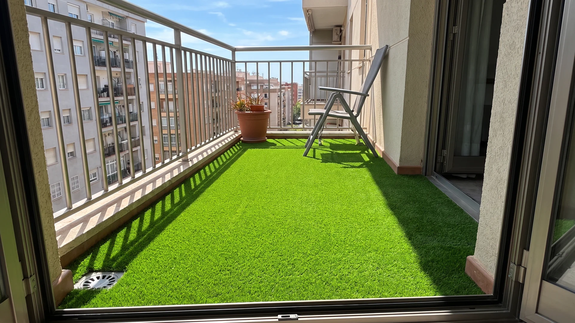 Balcón con césped artificial, silla, maceta y desagüe junto a la barandilla Balcón con césped artificial, silla, maceta y desagüe junto a la barandilla.
