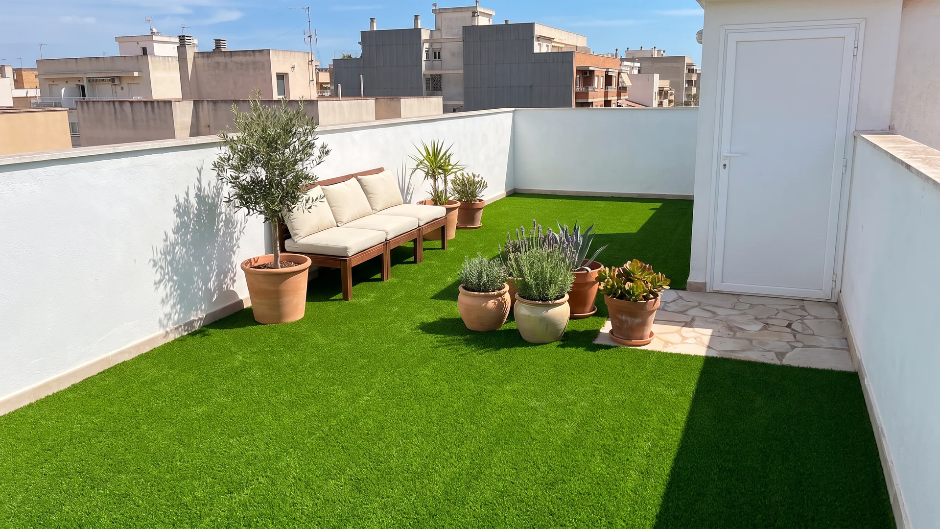 Terraza de ático con césped artificial, asiento y macetas junto a un acceso pavimentado Terraza de ático con césped artificial, asiento y macetas junto a un acceso pavimentado.