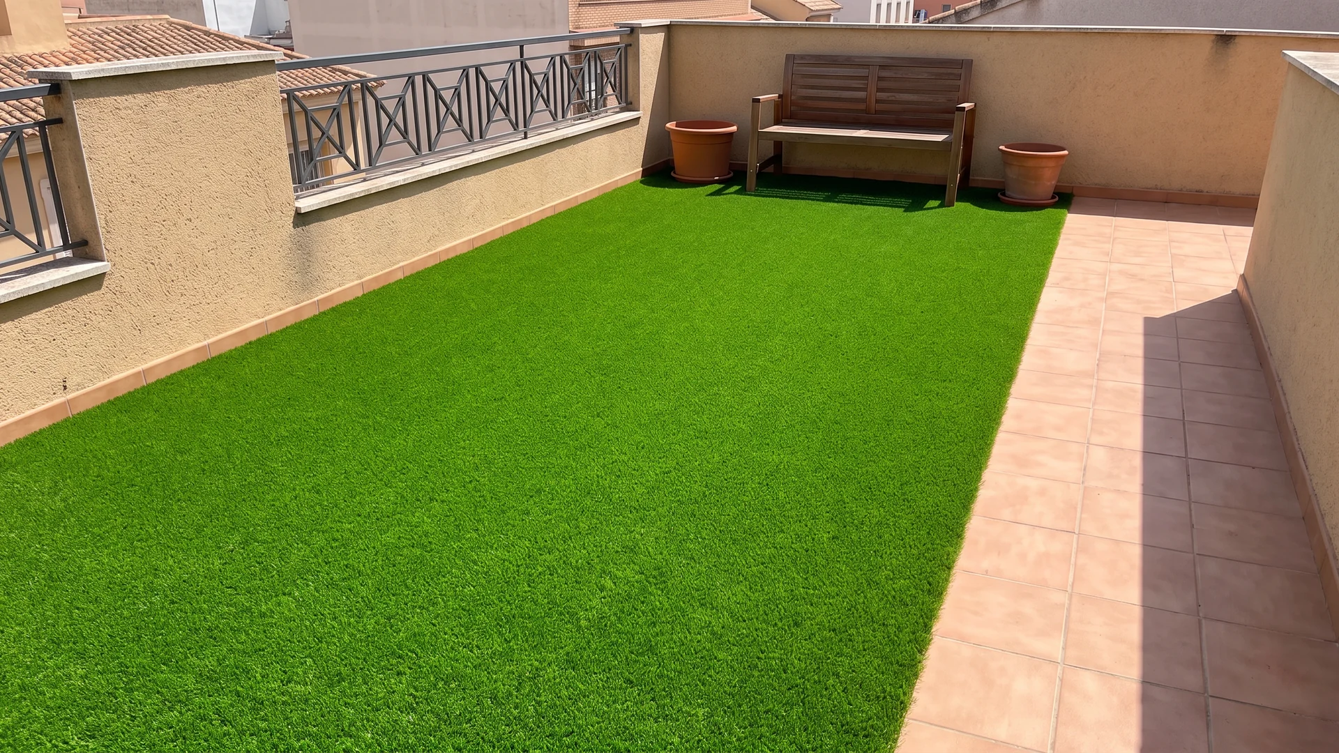 Terraza con césped artificial, banco y macetas junto a una barandilla Terraza con césped artificial, banco y macetas junto a una barandilla.