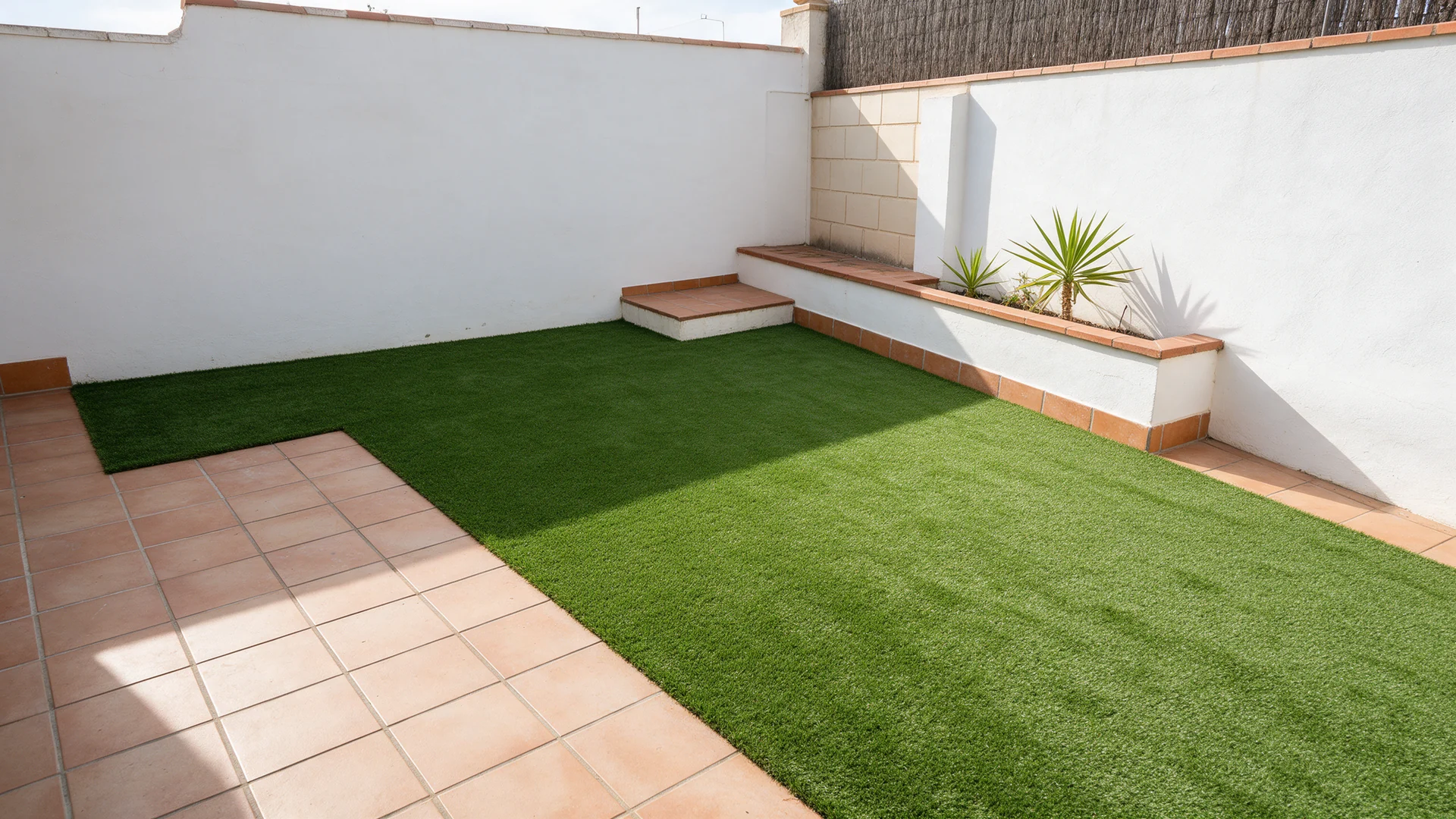 Patio con césped artificial en forma de L junto a pavimento cerámico.
