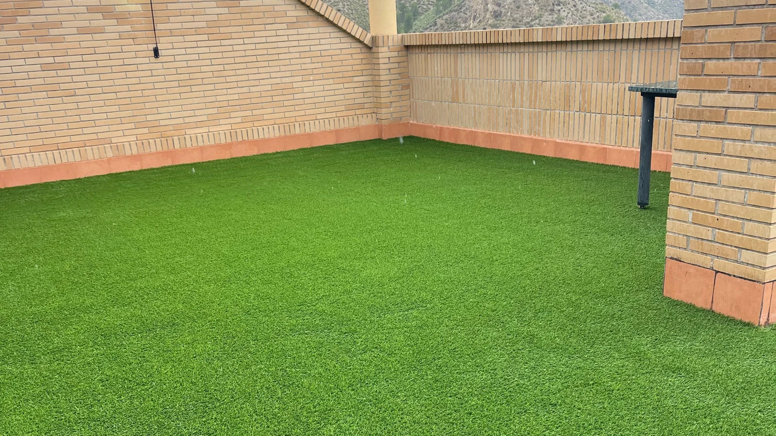 Césped artificial en ático, terraza con pérgola y muro de ladrillo