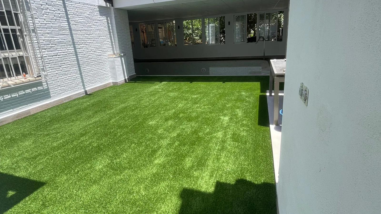 Césped artificial en ático, terraza junto a vivienda blanca
