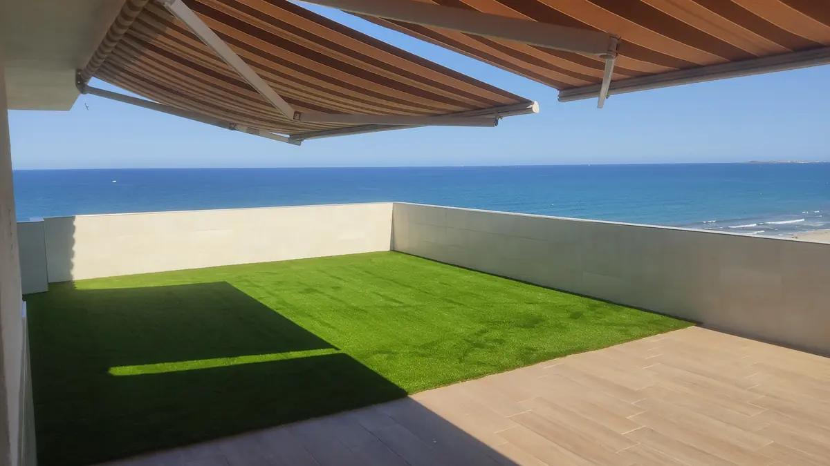 Terraza de ático con toldo y césped artificial frente al mar