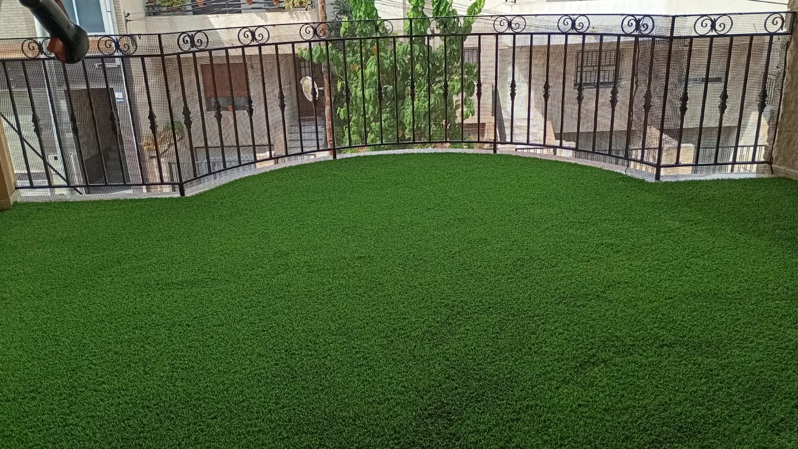 Césped artificial en balcón, barandilla metálica y vistas a viviendas