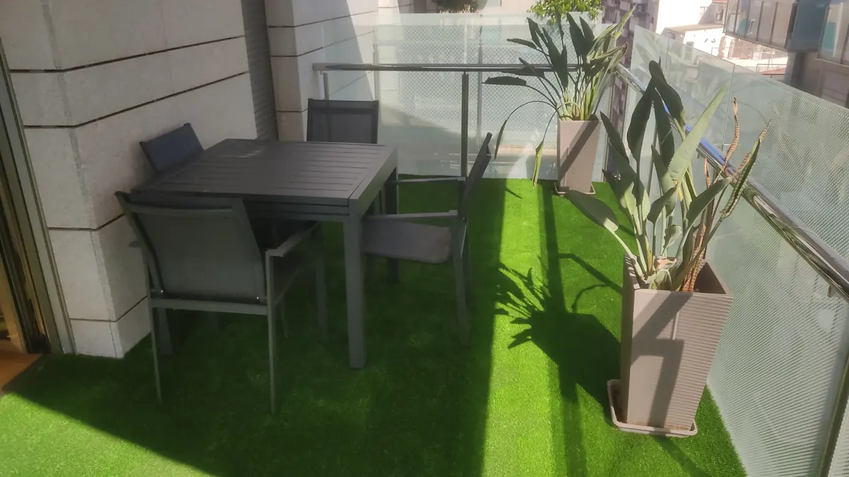 Balcón con césped artificial, mesa y barandilla de cristal