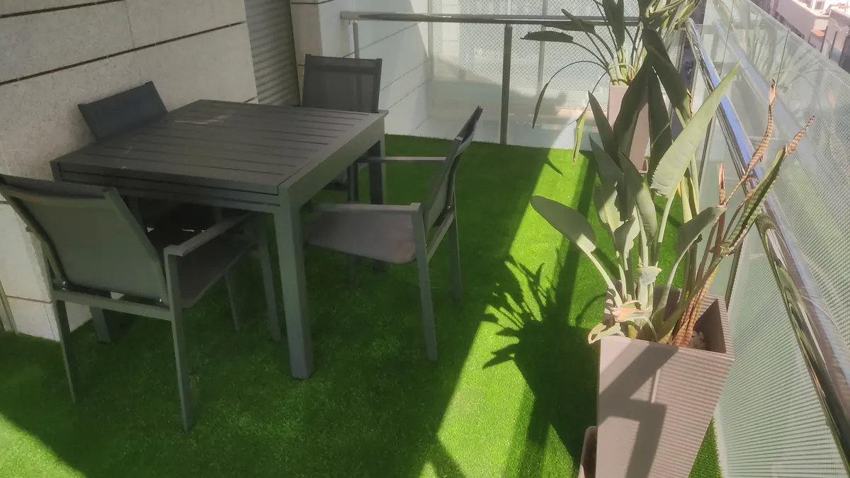 Balcón con césped artificial, mesa de exterior y maceta