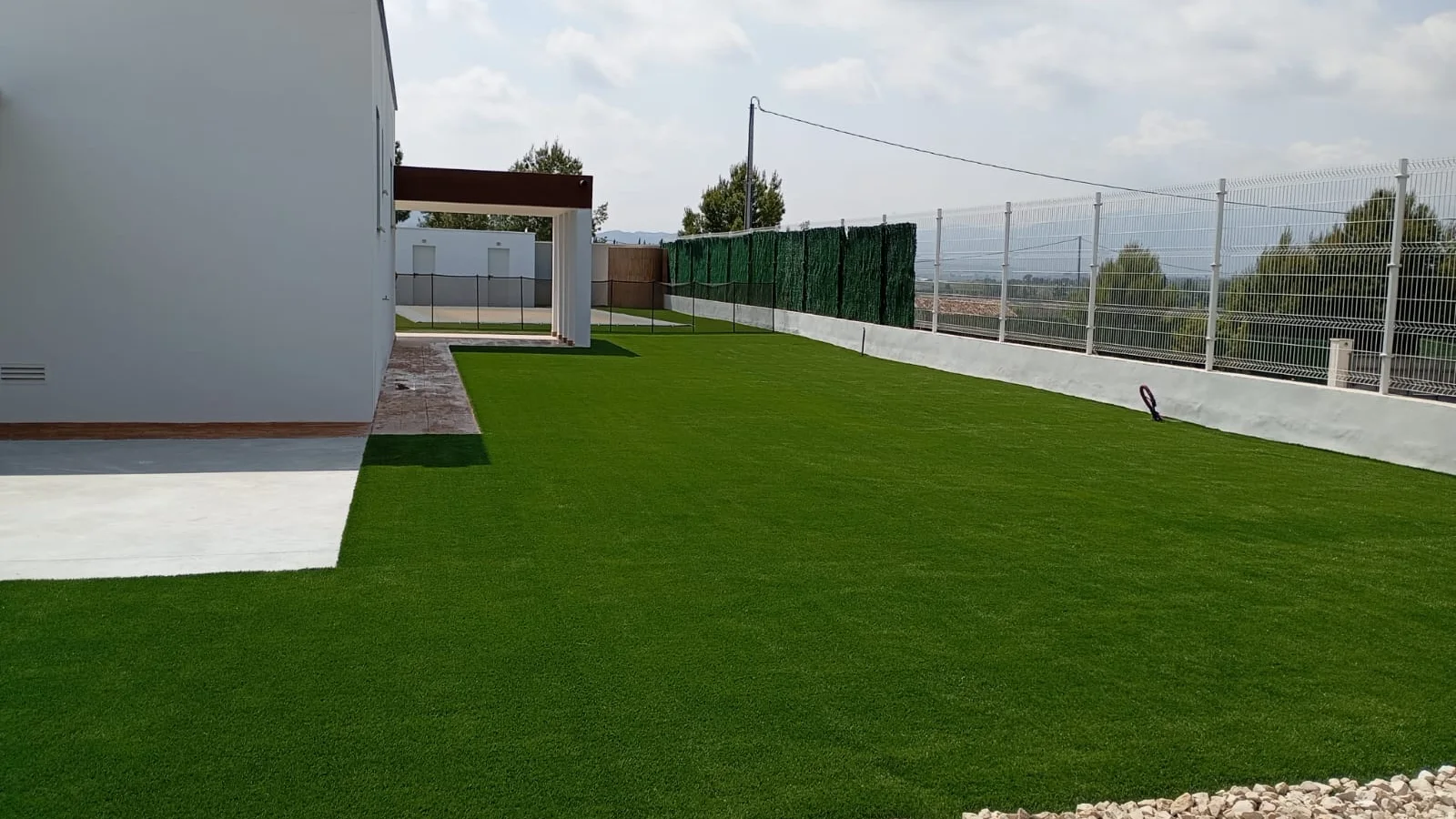 Césped artificial en jardín, vivienda blanca y vistas abiertas