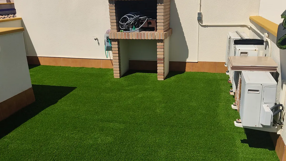 Terraza de ático con césped artificial y barbacoa de obra