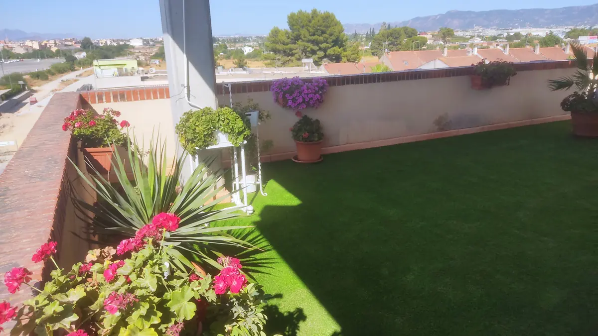 Terraza de ático con césped artificial, flores y vistas urbanas
