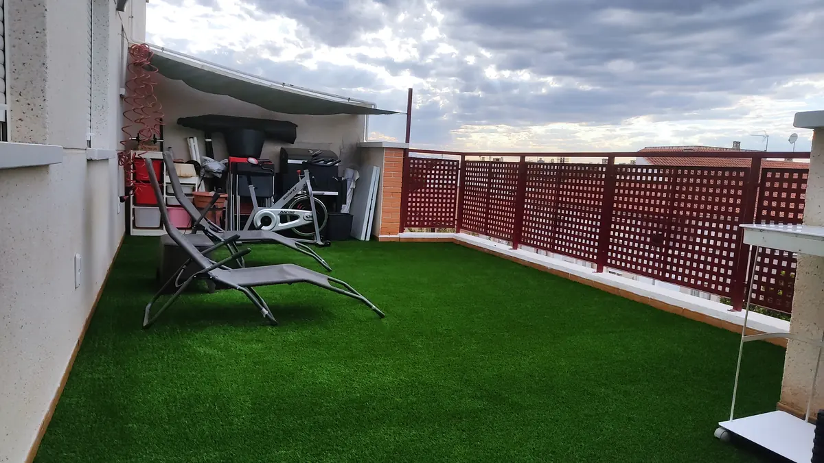 Terraza de ático con césped artificial, tumbonas y celosía roja