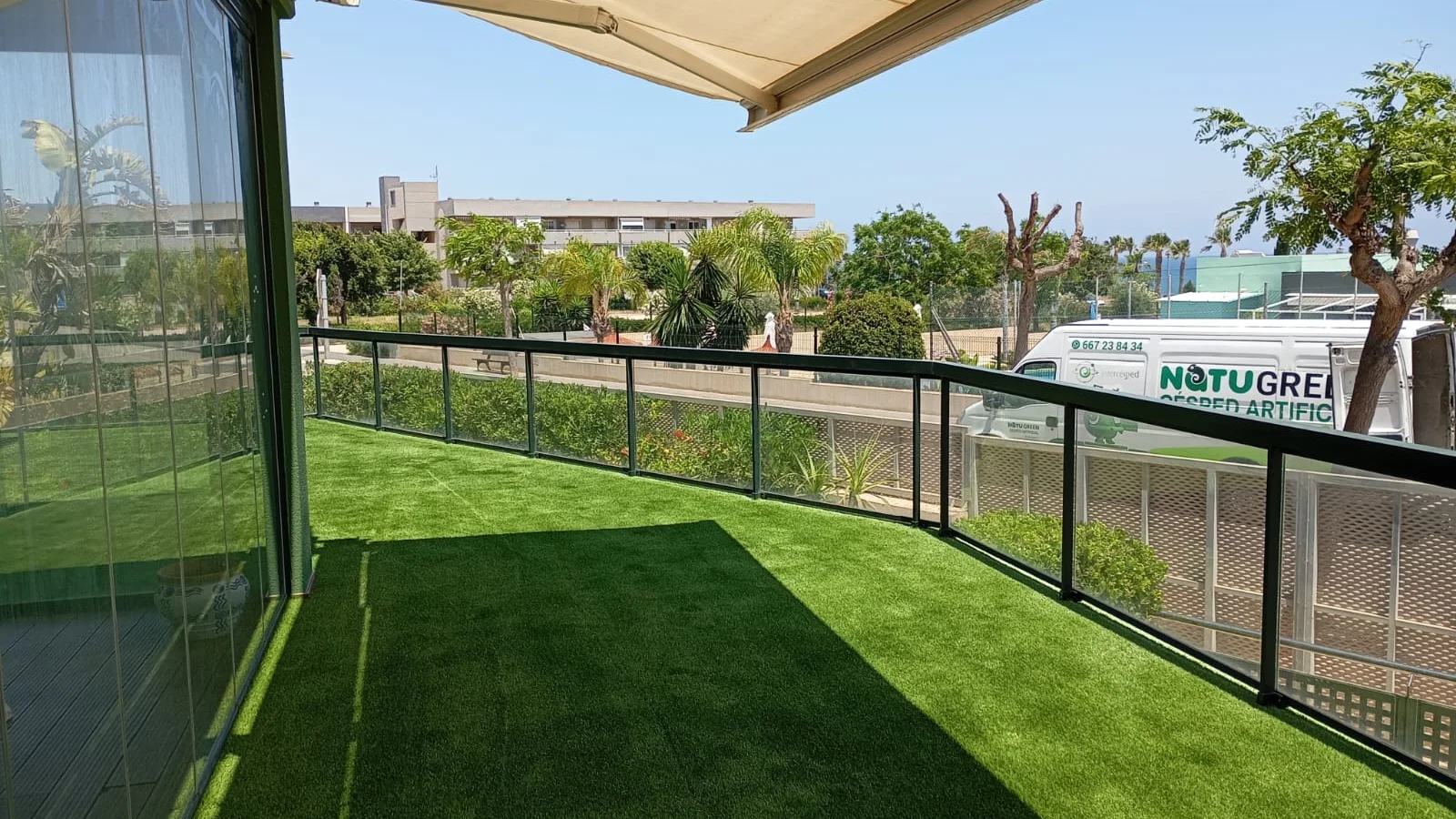 Césped artificial en terraza, toldo y barandilla de cristal